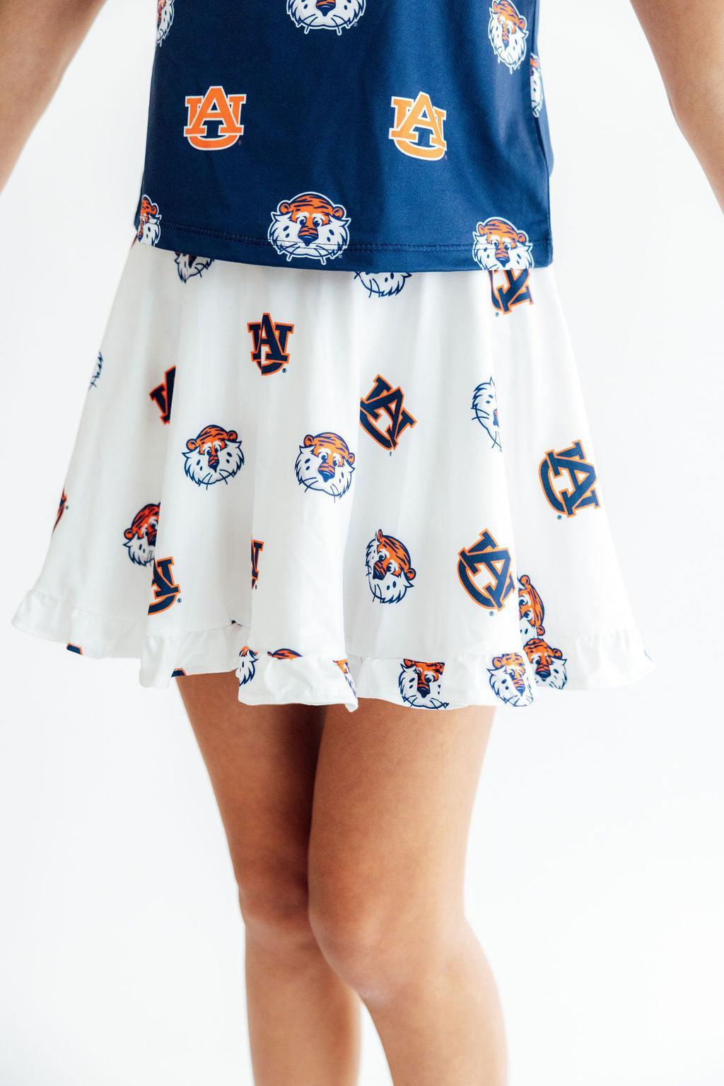A child wearing a navy blue top and white skirt set with repeating Auburn Tigers and Auburn 'AU' logo prints, shown from the torso down against a plain white background.