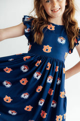 A young girl wearing a navy blue dress with an all-over Auburn Tigers logo print, shown from the waist up against a plain white background.