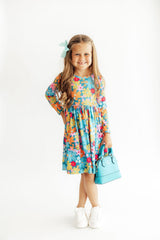 Young girl wearing a colorful floral dress holding a blue handbag on a white background