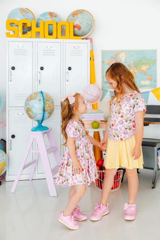 Two young girls standing in a classroom setting with educational decor.