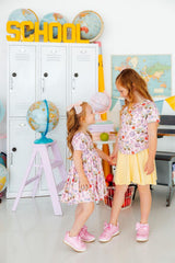 Two young girls standing in a classroom setting with educational decor.