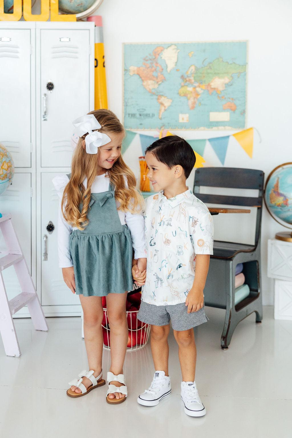 Two children standing in a room with educational decor, including a world map and globes.
