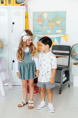 Two children standing in a room with educational decor, including a world map and globes.