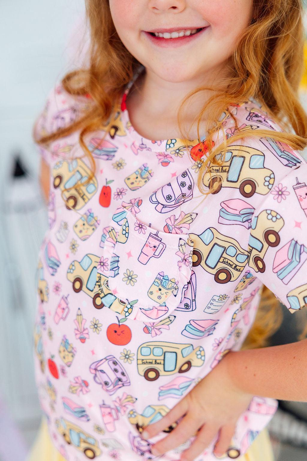Child wearing a pink apron with colorful vehicle patterns.