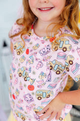 Child wearing a pink apron with colorful vehicle patterns.