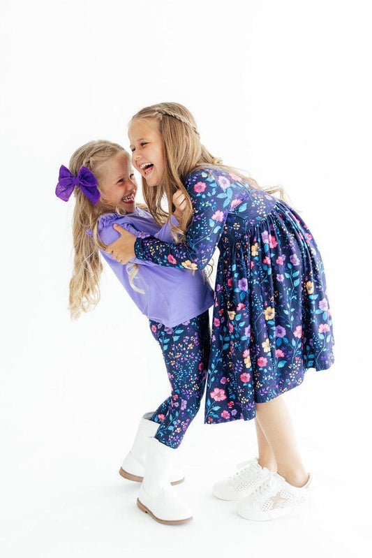 Two children in matching floral outfits with purple accents on a white background