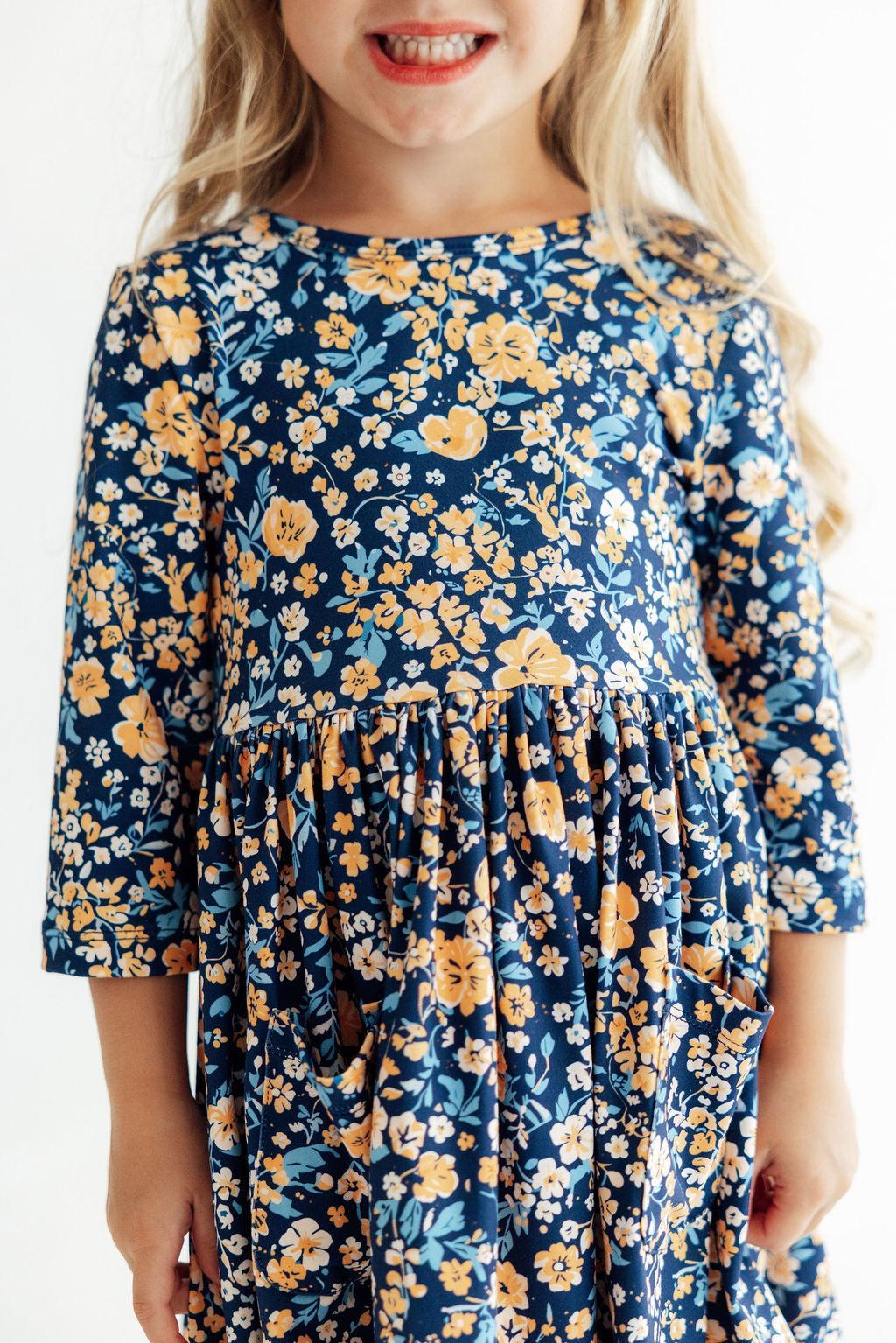 Child wearing a navy floral dress with yellow flowers on a white background