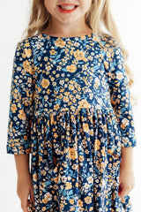 Child wearing a navy floral dress with yellow flowers on a white background