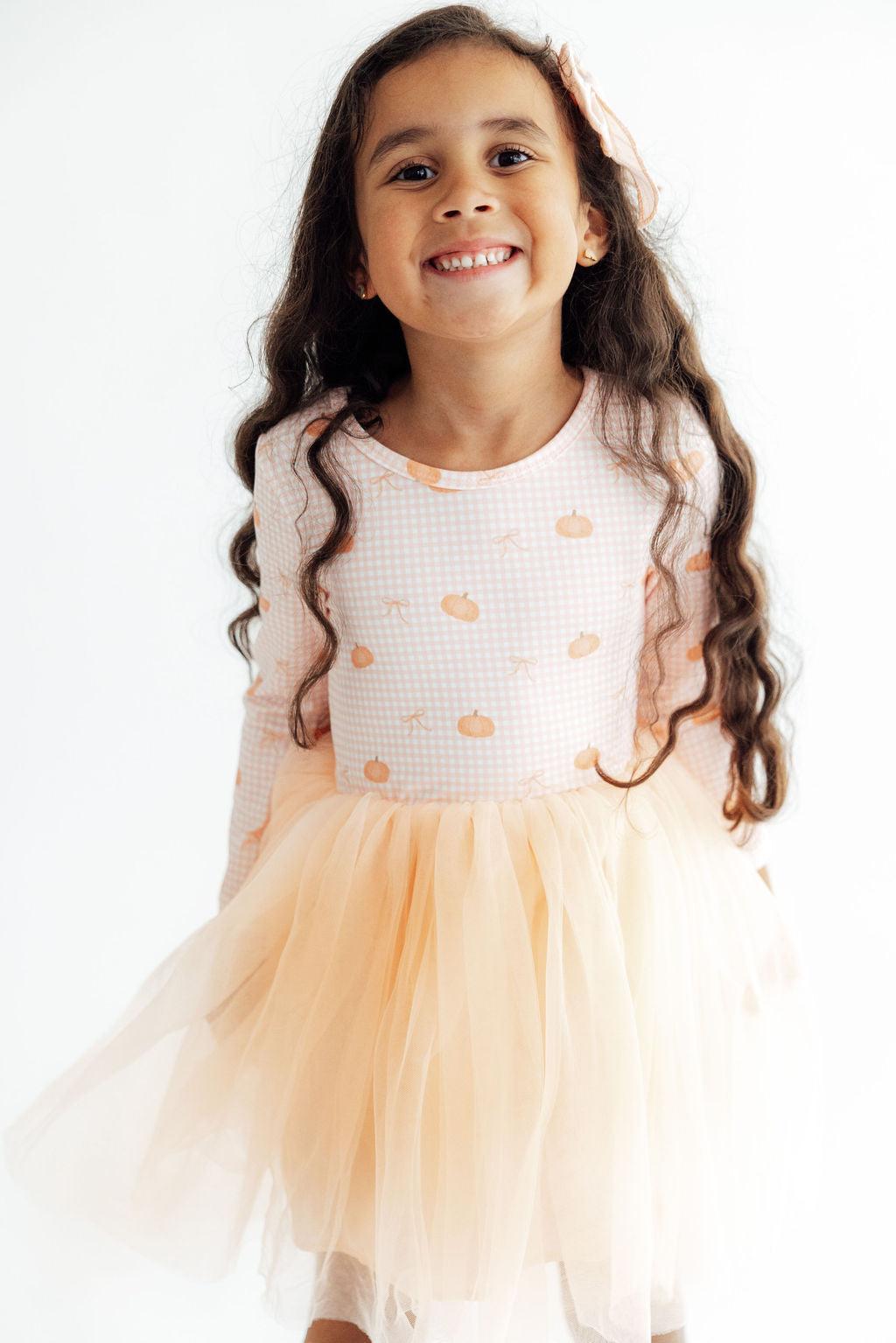 Young girl wearing a white top with orange patterns and a peach-colored tutu skirt on a white background