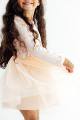 Child wearing a white sweater with floral patterns and a peach skirt on a white background