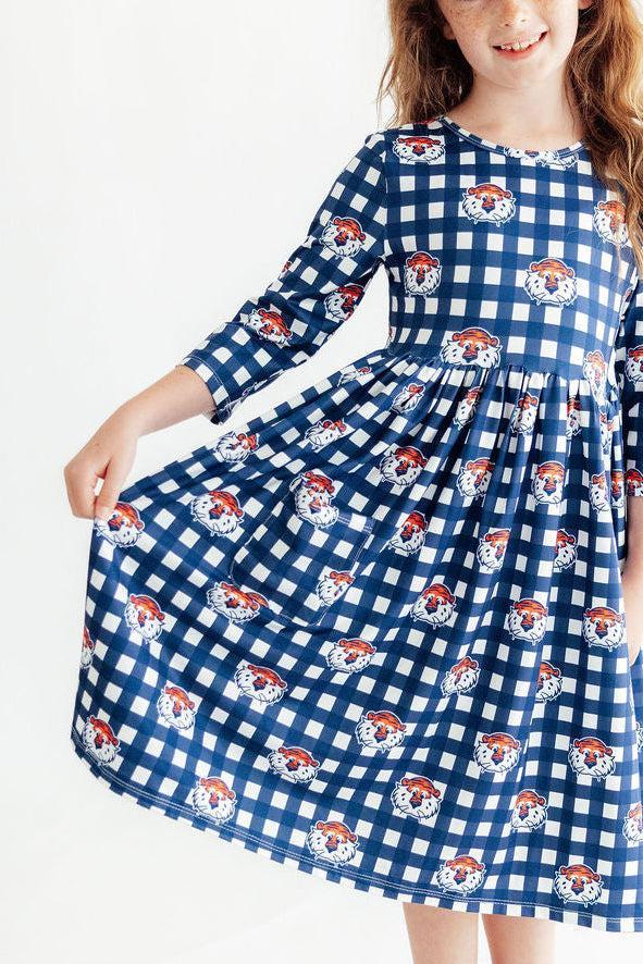 A young girl wearing a blue and white gingham dress with a repeating pattern of cartoon dog faces, shown against a plain white background.