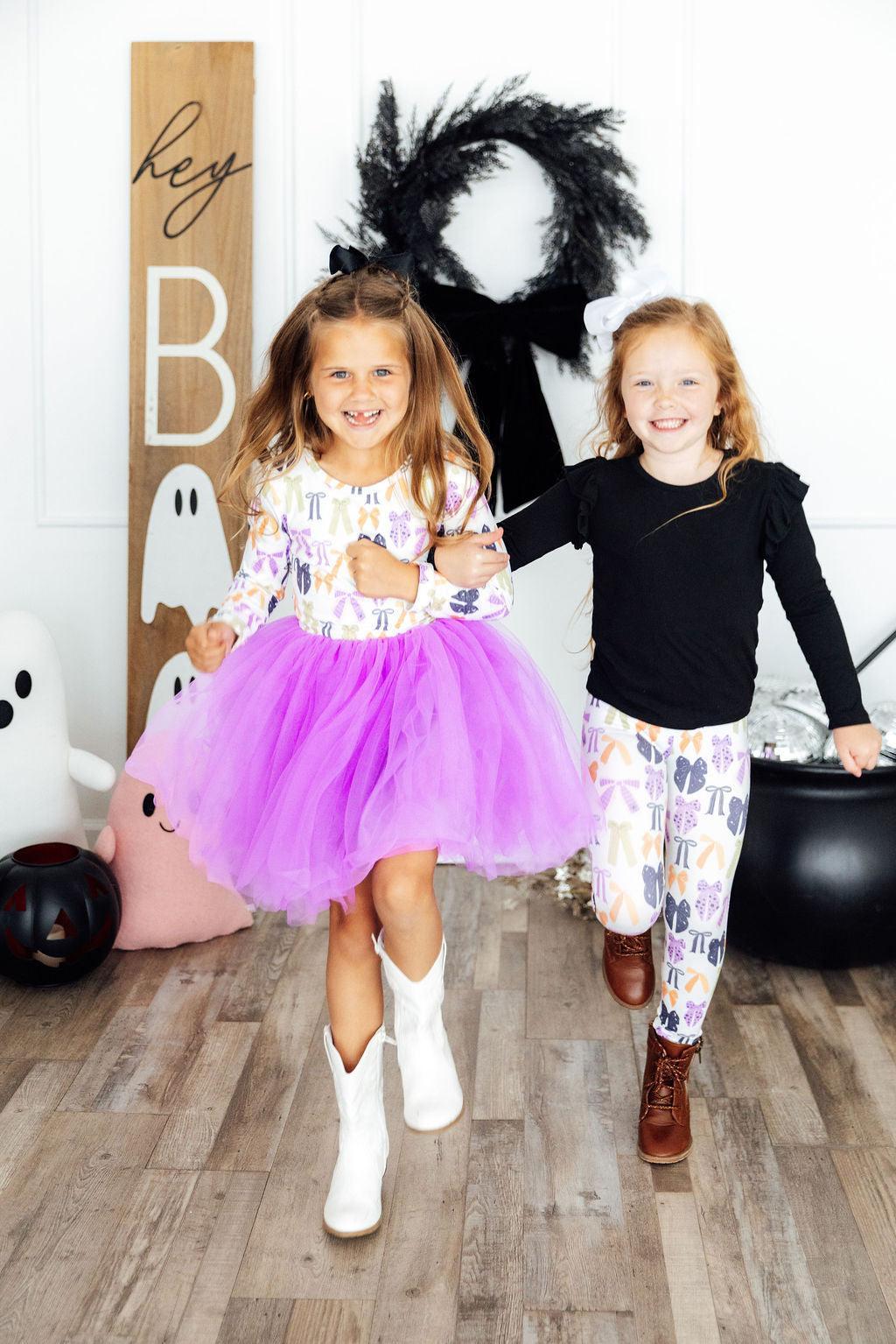 Two children in Halloween costumes standing in a decorated room with pumpkins and a sign.