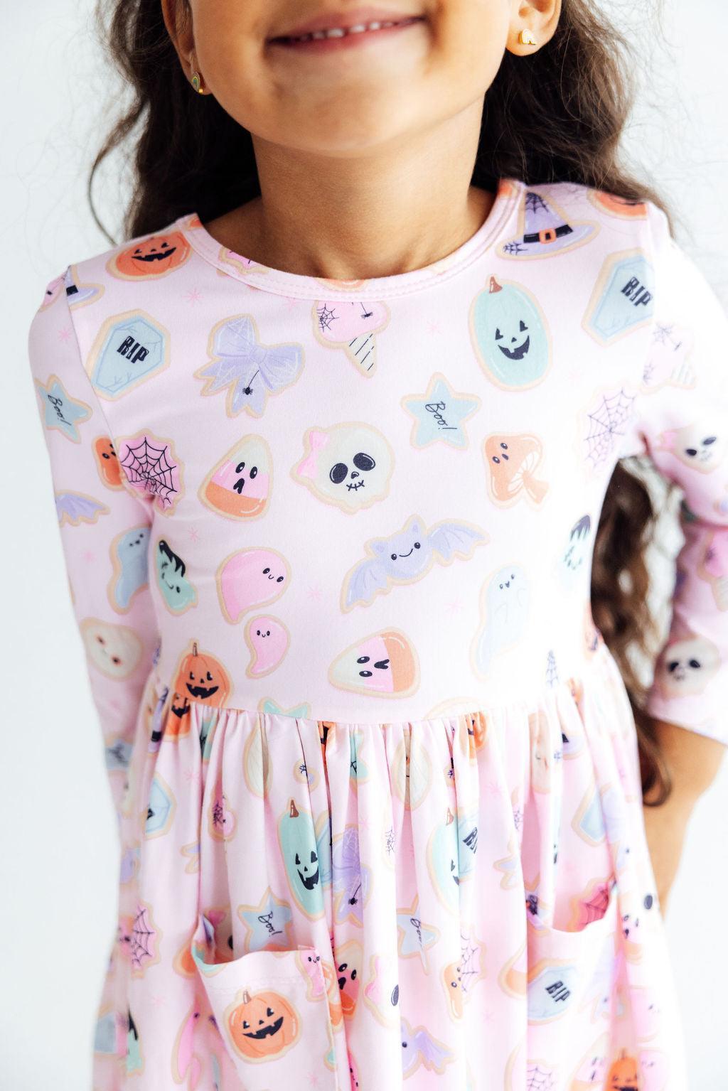 Child wearing a dress with Halloween-themed ghost and pumpkin print.
