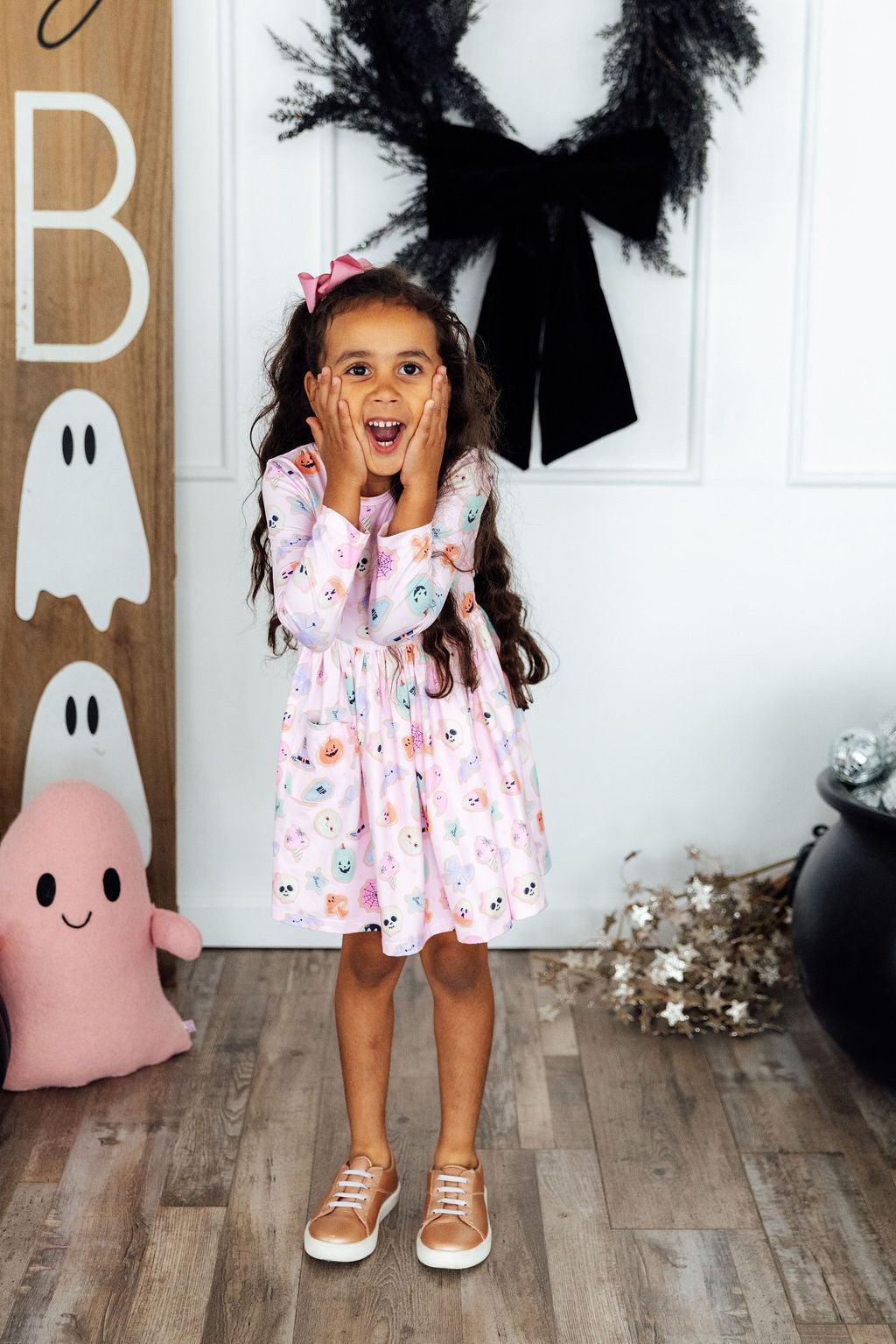 Young girl in a floral dress standing in front of Halloween decorations.