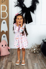 Young girl in a floral dress standing in front of Halloween decorations.