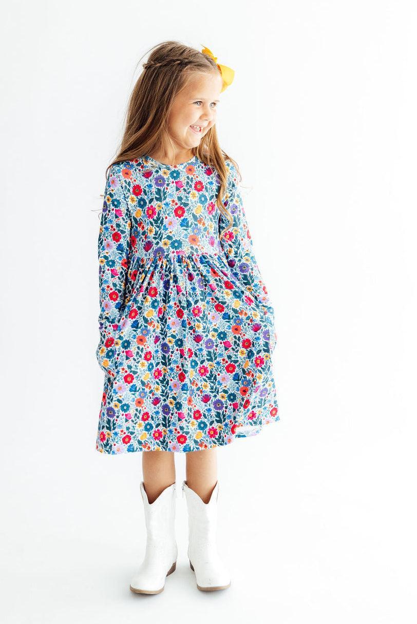 Young girl wearing a colorful floral dress with white boots on a white background