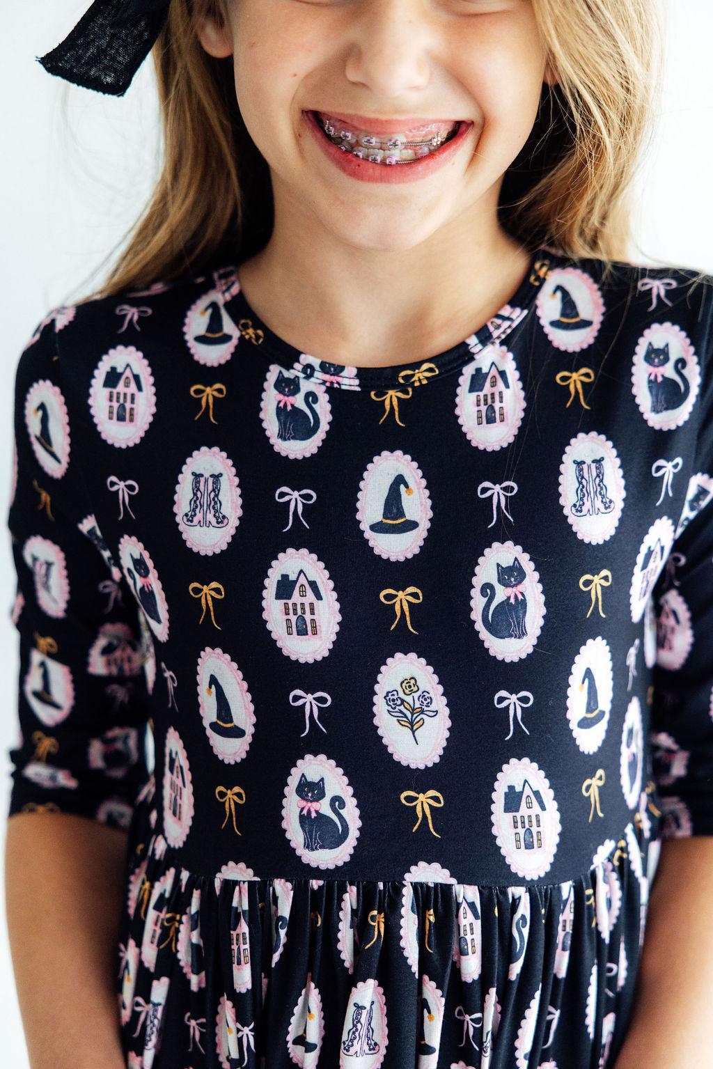 Child wearing a dress with a pattern of cats, houses, and bows on a navy background.