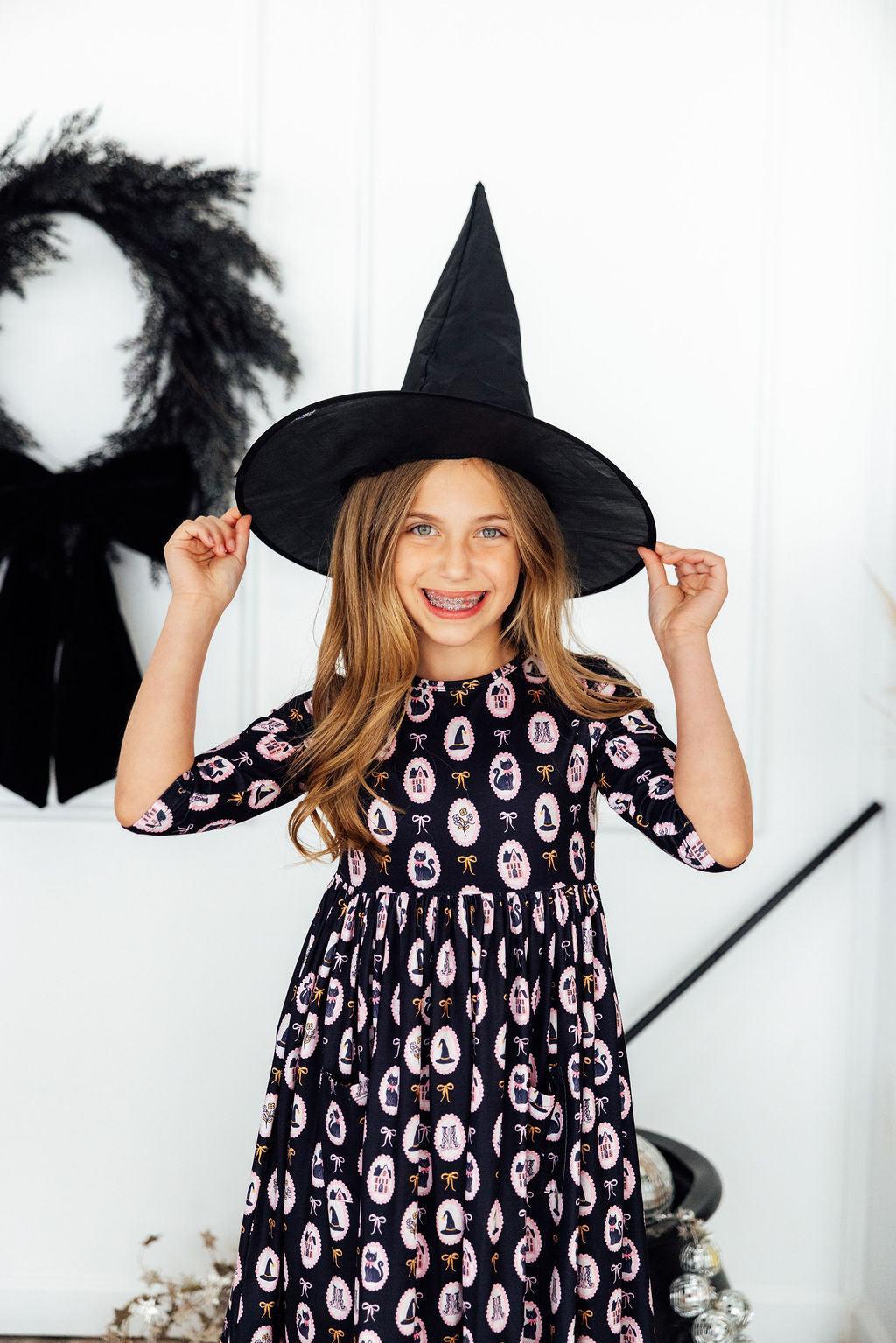 Child wearing a witch hat and patterned dress in a Halloween-themed setting