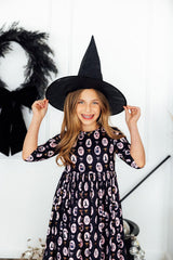 Child wearing a witch hat and patterned dress in a Halloween-themed setting