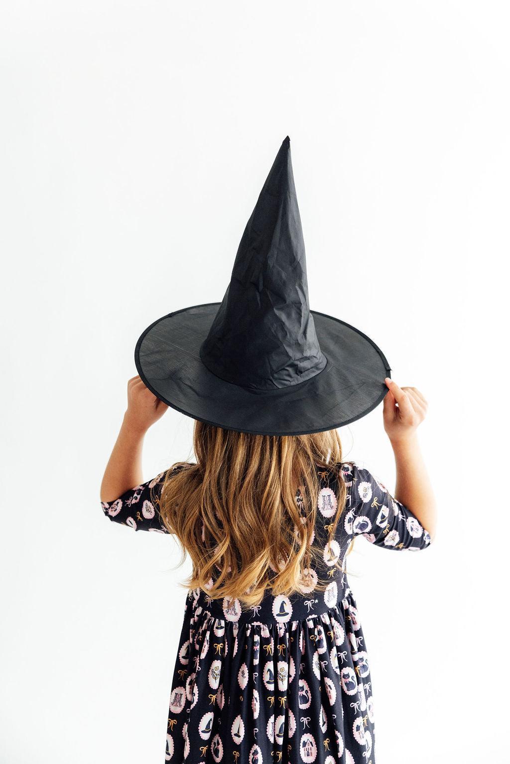 Person wearing a black witch hat and patterned dress on a white background