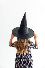 Person wearing a black witch hat and patterned dress on a white background