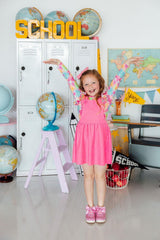 Child in a pink dress standing in a classroom with globes and lockers.