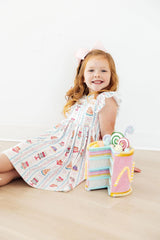 Young girl sitting on a beige surface with colorful plush toys next to her.