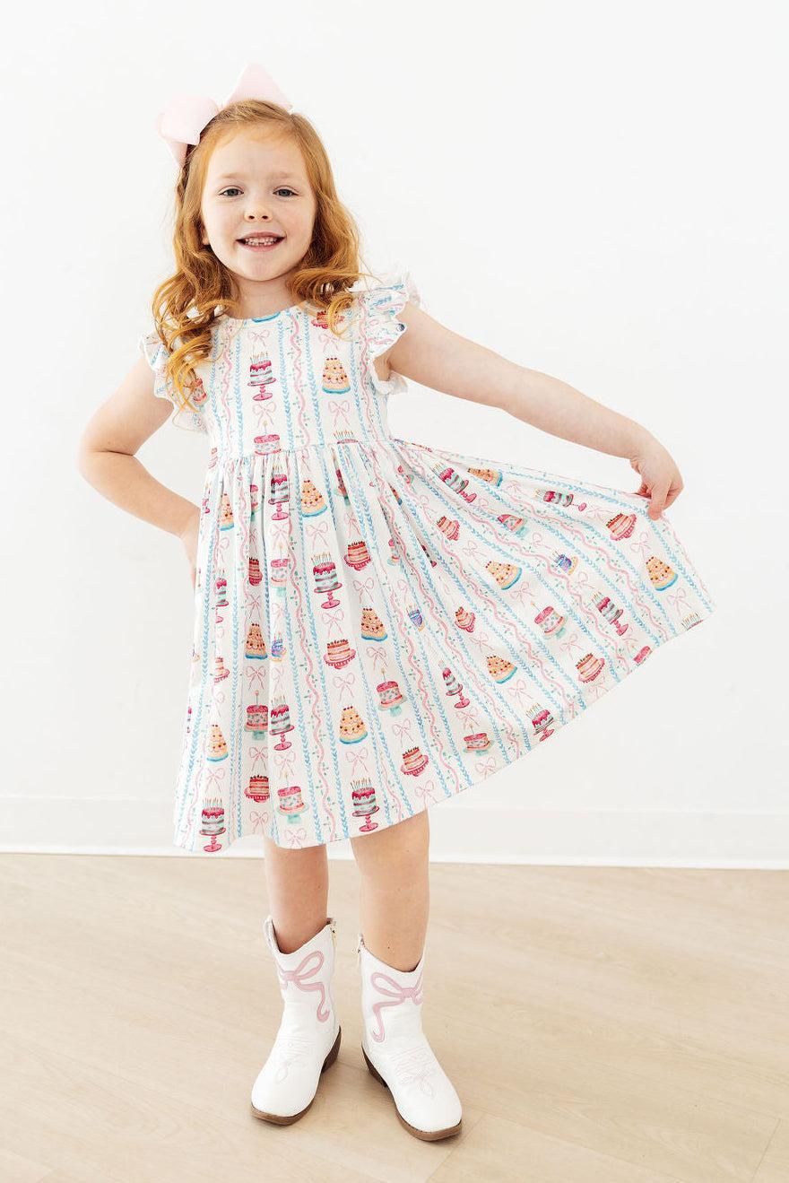 Young girl wearing a dress with a pattern of cars and trees on a white background