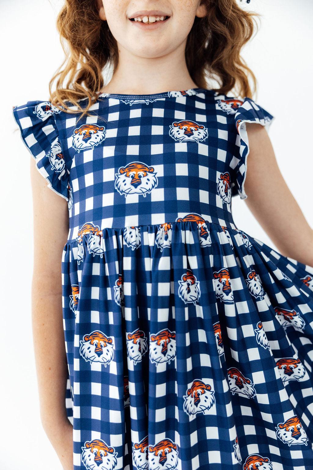 A young girl wearing a navy and white gingham dress with a repeating print of tiger faces, shown from the shoulders down against a plain white background.