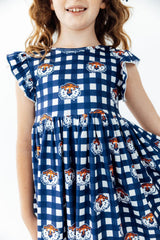 A young girl wearing a navy and white gingham dress with a repeating print of tiger faces, shown from the shoulders down against a plain white background.
