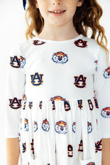 A young girl wearing a white long-sleeve dress with an all-over Auburn Tigers logo and tiger head print, shown from the shoulders down against a clean white background.