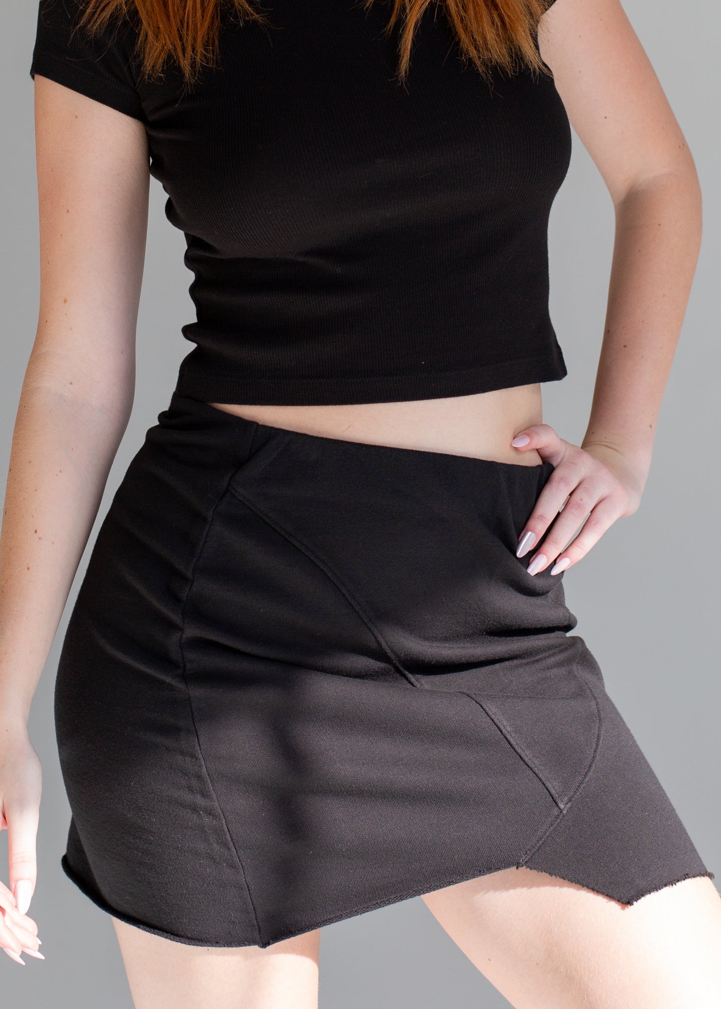Person wearing a black crop top and black skirt on a gray background