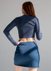 Woman wearing a blue long-sleeve top and skirt against a gray background