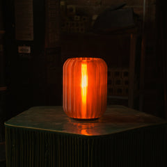 Orange ribbed glass table lamp on a dark surface with a blurred background
