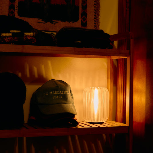 Cap with 'La Maddalena Italy' text on a wooden shelf with a lamp casting a warm glow.
