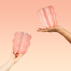 Two hands holding pink and white striped pouches against a peach background