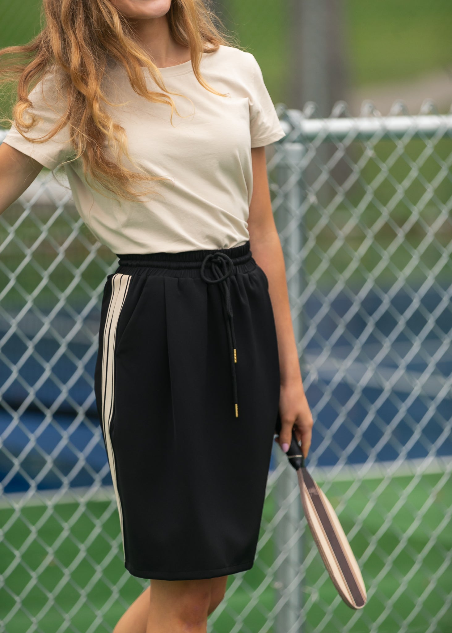 Person wearing a white top and black skirt with a tennis racket on a tennis court.