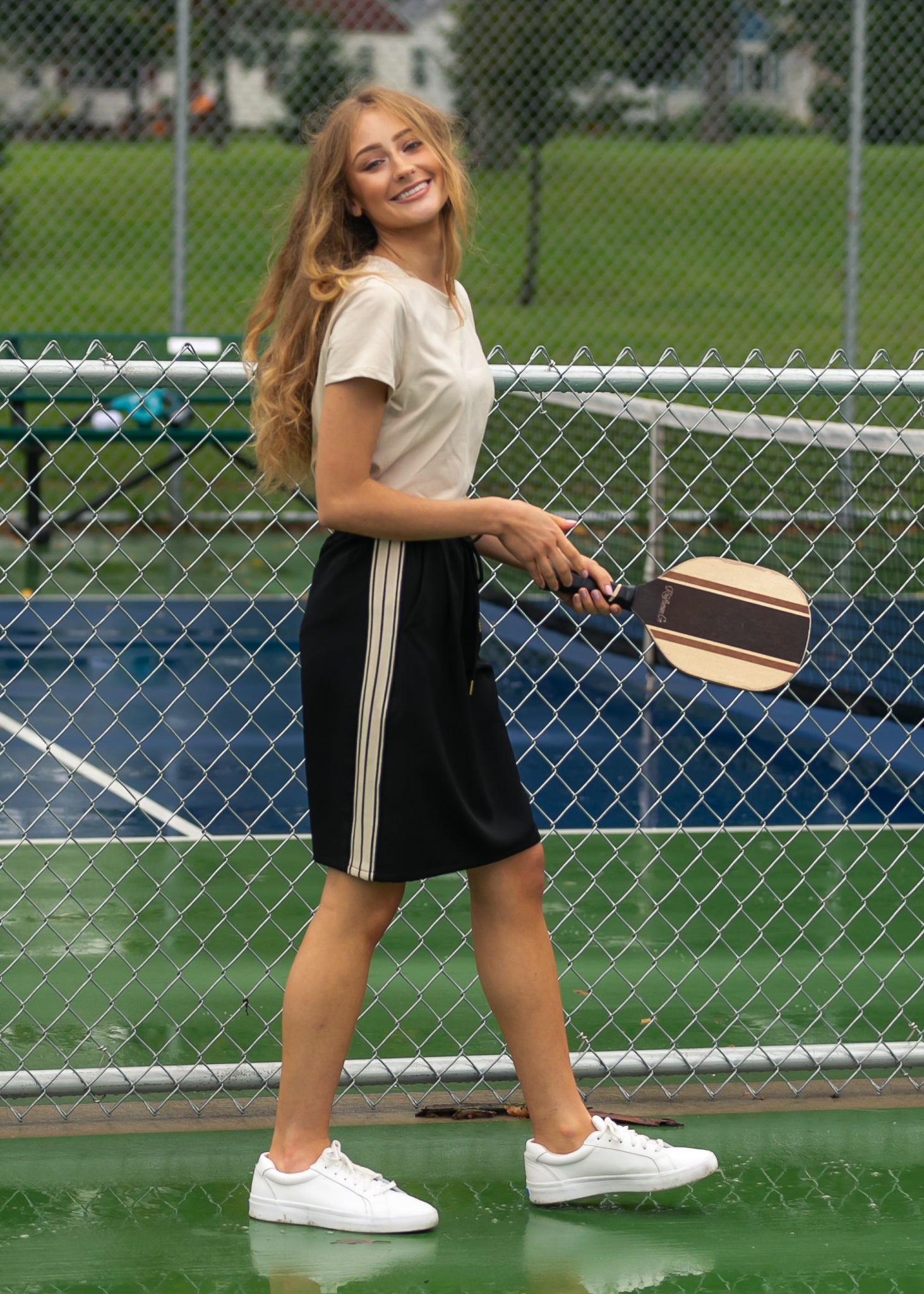 Woman holding a paddle on a tennis court with a chain-link fence in the background