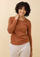 Woman wearing a brown long-sleeve top and white pants against a beige background
