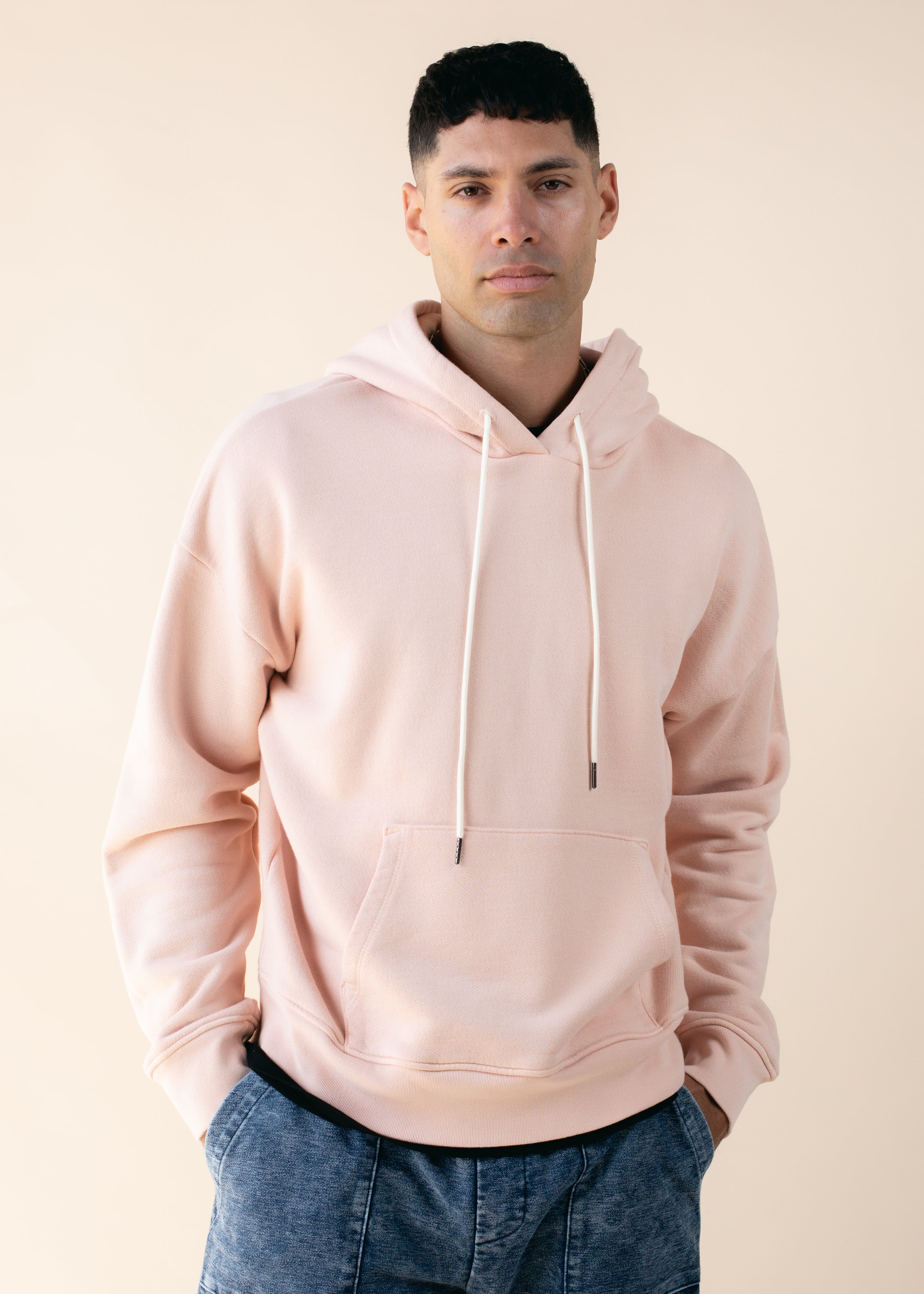 Man wearing a light pink hoodie against a beige background