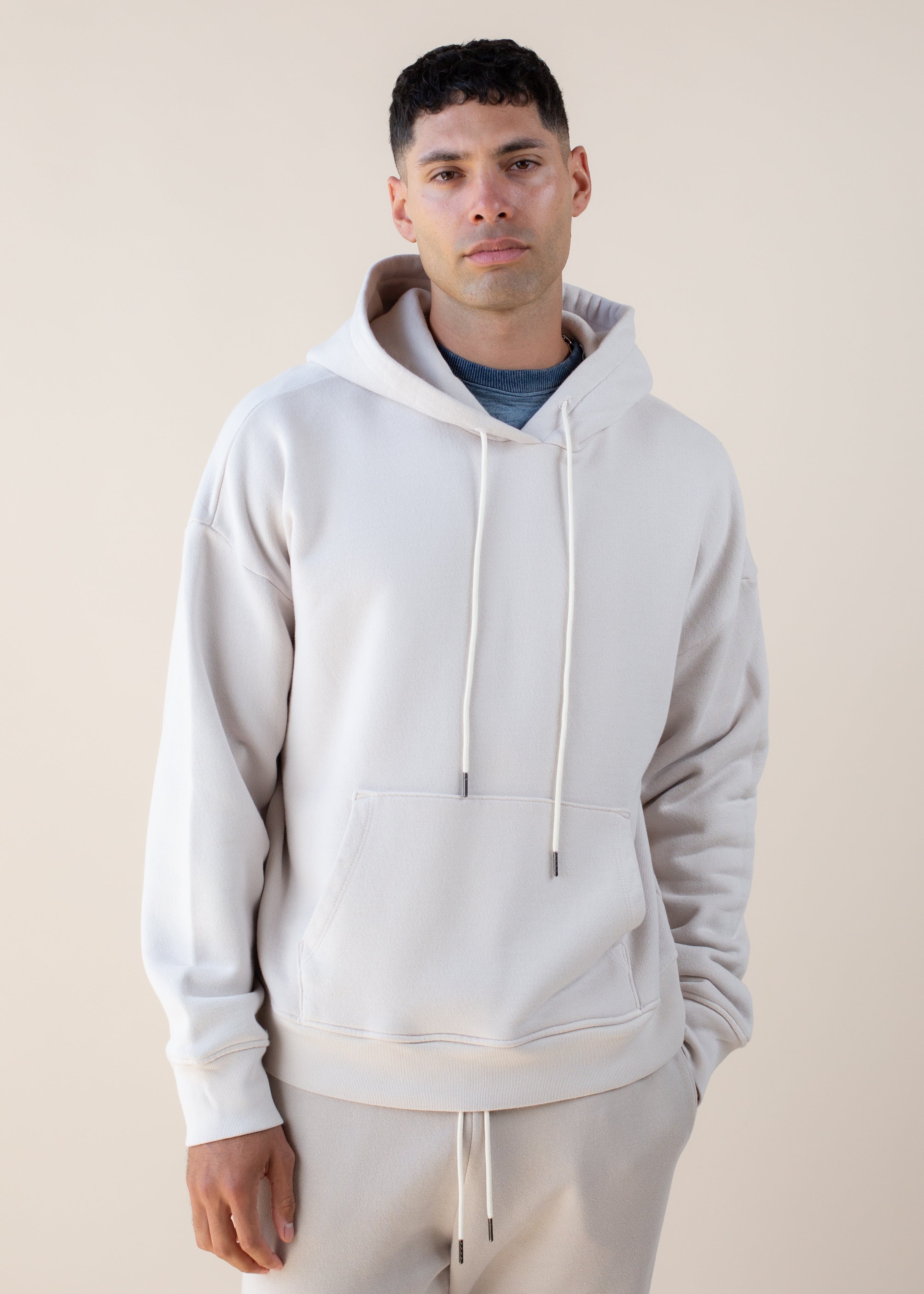 Man wearing a light gray hoodie and beige pants against a plain background