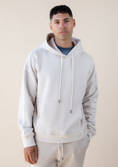 Man wearing a light gray hoodie and beige pants against a plain background