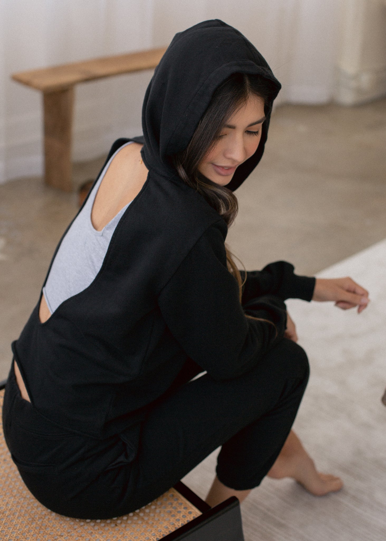Woman wearing a black hoodie with cut-out shoulders in a minimal indoor setting
