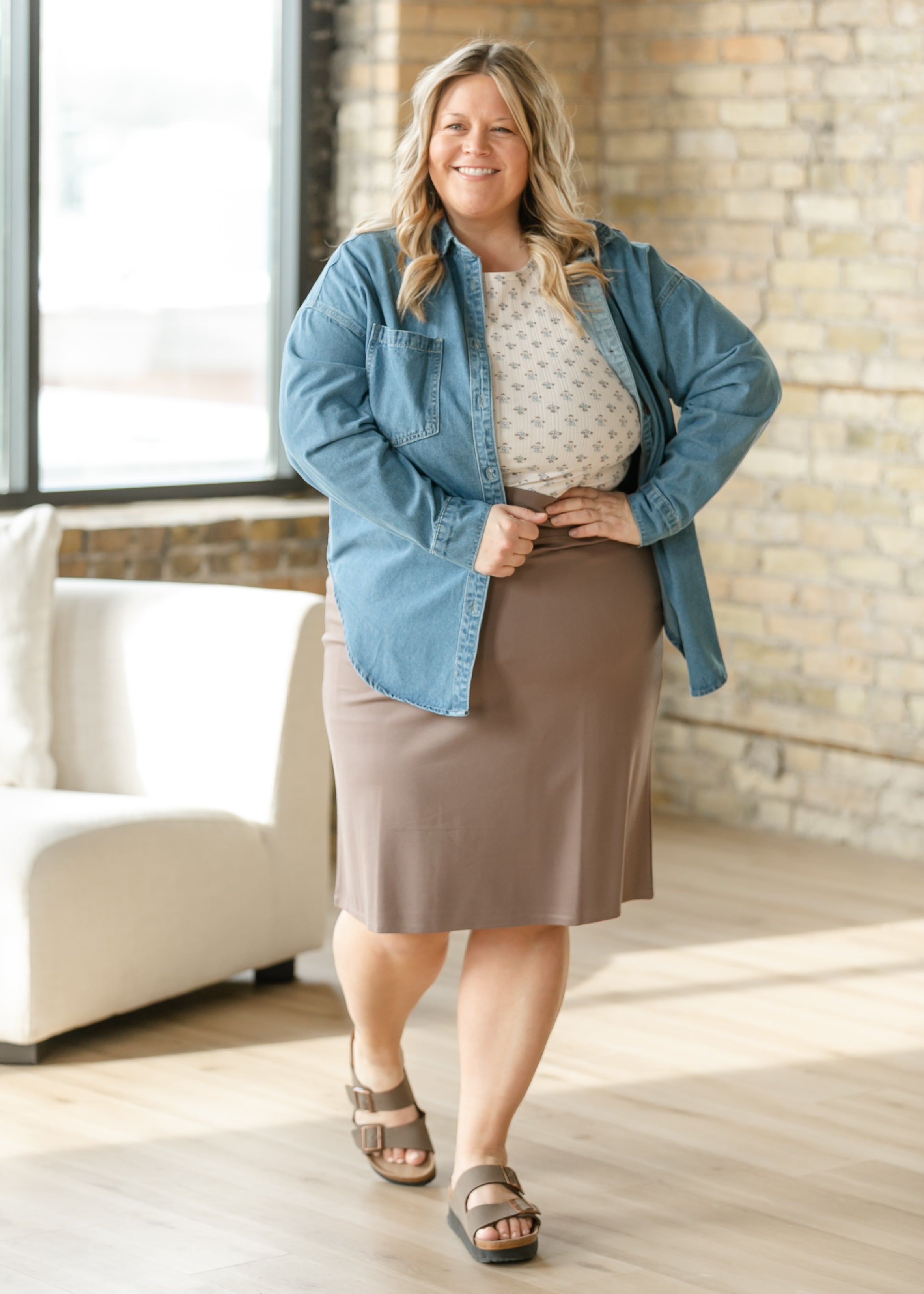 Woman wearing a denim jacket over a beige skirt in a well-lit room.