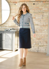 Woman wearing a striped sweater and navy skirt in a room with a stone wall.