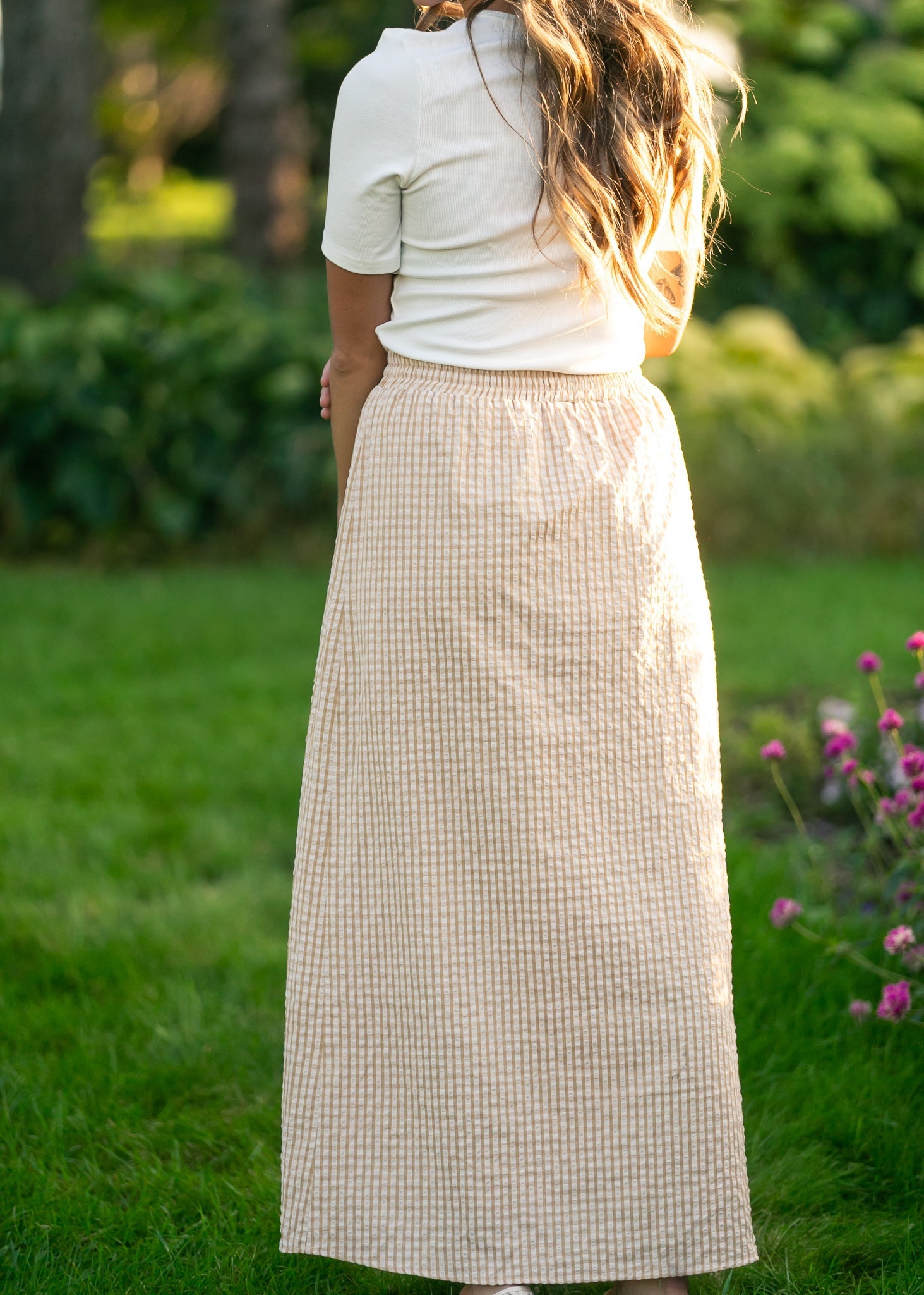 Person wearing a long beige checkered skirt in a garden setting