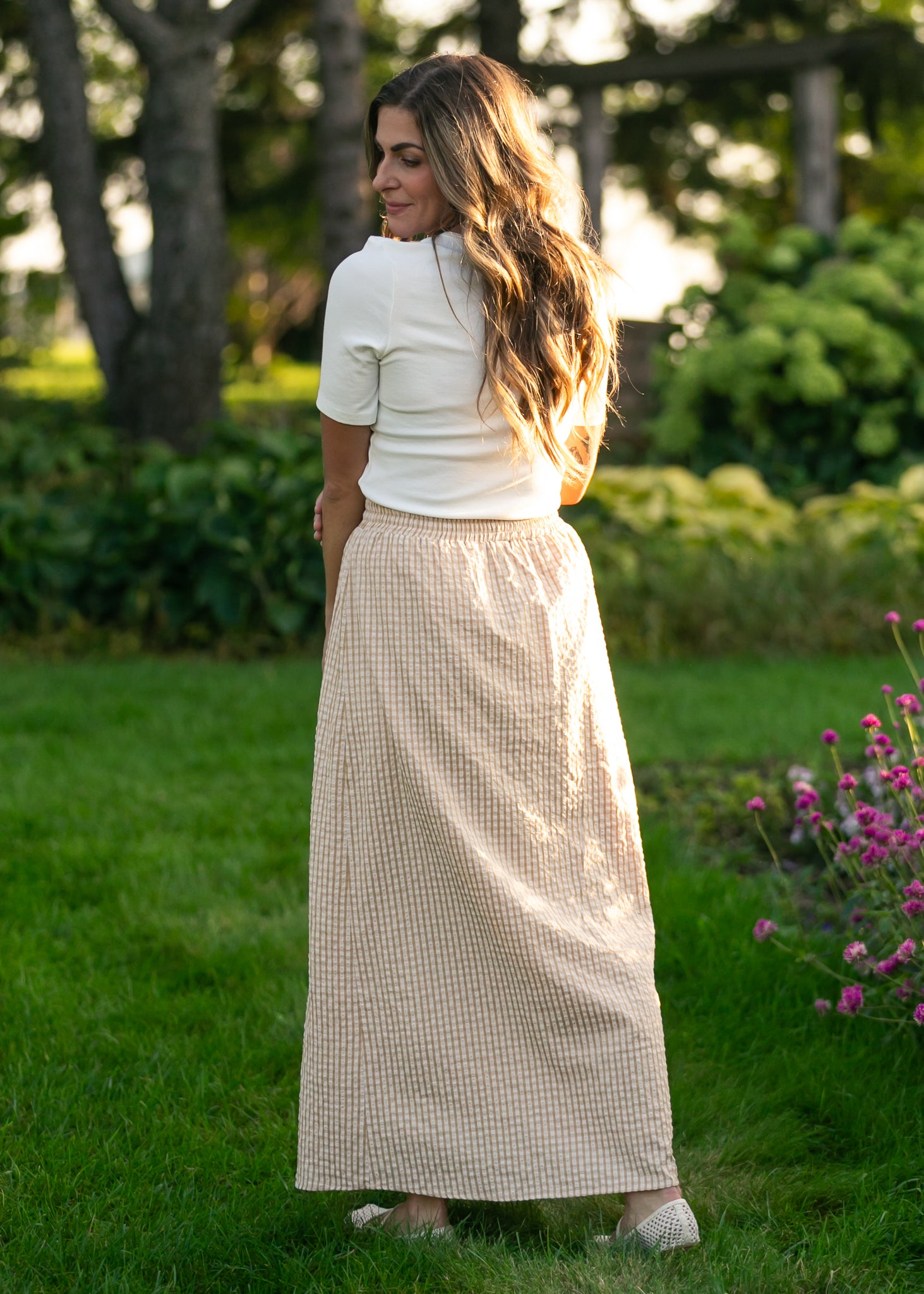 Woman in a white top and beige checkered skirt standing in a garden.