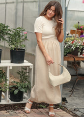 Woman in a beige top and plaid skirt holding a matching handbag in a garden setting.