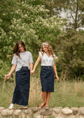 Two women walking hand in hand on a stone path with trees in the background