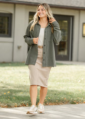 Woman wearing a green shirt and beige skirt standing outdoors.